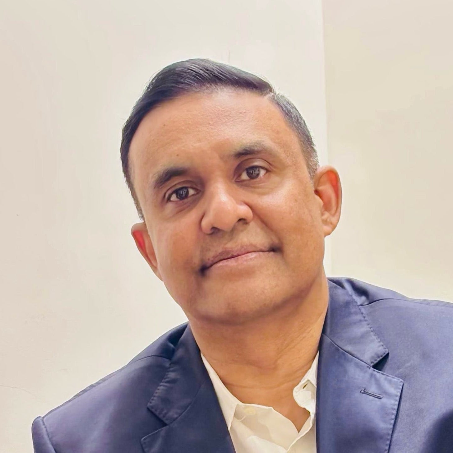 Man wearing a blue blazer over a white shirt against a plain background